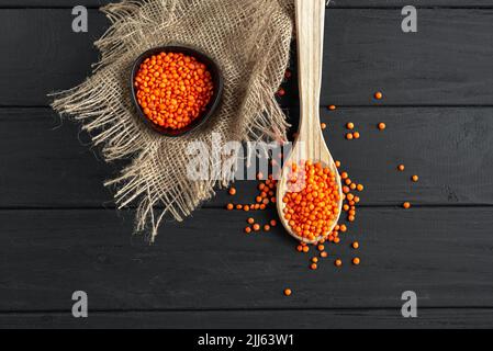 Rote Linsen auf einem rustikalen dunklen Holzhintergrund. Müslisentilen auf einem Holzlöffel. Uralte Getreideprodukte Stockfoto