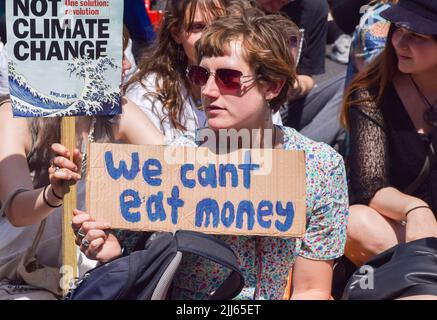 London, England, Großbritannien. 23.. Juli 2022. Ein Protestler hält auf dem Parliament Square ein Plakat mit der Aufschrift „Wir können kein Geld essen“. Demonstranten von Just Stop Oil, Extinction Rebellion, Isolate Britain und anderen Gruppen veranstalteten einen marsch durch das Zentrum Londons, in dem sie die Regierung aufforderten, fossile Brennstoffe zu beenden, große Umweltverschmutzer und Milliardäre zu besteuern, alle Häuser zu isolieren und gegen das Klima und die Lebenshaltungskosten zu handeln. (Bild: © Vuk Valcic/ZUMA Press Wire) Stockfoto