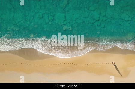 Frau geht am Strand entlang brechender Wellen und hinterlässt Spuren auf dem Sand. Luftaufnahme direkt darüber Stockfoto