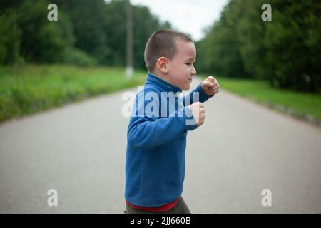 Das Kind ist wütend. Junge droht. Schuljunge schwört auf der Straße. Negative Emotionen beim Kind. Stockfoto