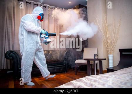 Desinfektion des Raumes gegen Viren. Mann in Quarantänekleidung, der den Raum desinfiziert. Stockfoto