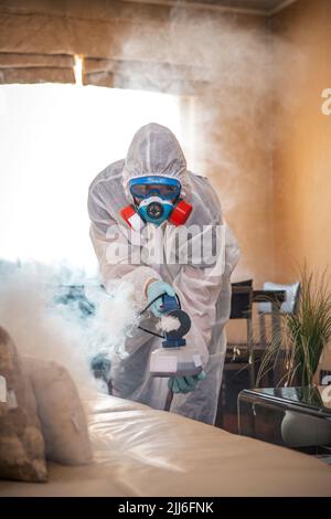 Desinfektion des Raumes gegen Viren. Mann in Quarantänekleidung, der den Raum desinfiziert. Stockfoto