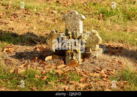 Eine Nahaufnahme eines gebrochenen Kreuzes, das im Herbst liegt, hinterlässt einen ruhigen Friedhof Stockfoto