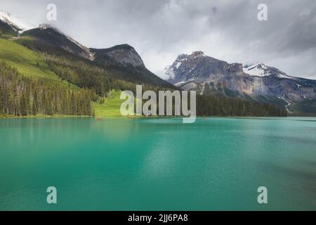 Berglandschaft und Touristen in bunten roten Kanus während eines friedlichen Morgens auf Emerald Lake im Yoho Nationalpark, in British Columbia, Kanada. Stockfoto