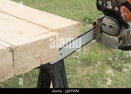 Ein Bauarbeiter schneidet Bretter mit einer Kettensäge in der Konstruktion. Konzentrieren Sie sich auf Kettensäge Stockfoto