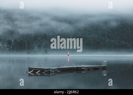 Moody, atmosphärischer Abendnebel über schwimmenden Doch und Wharf am malerischen Kootenay Lake in Nelson, BC, Kanada. Stockfoto