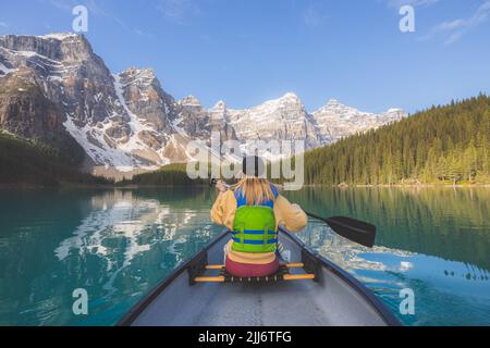 Eine junge blonde Frau paddelt mit dem Kanu auf dem malerischen, glazialen Moraine Lake, einem beliebten Touristenziel im Banff National Park, Al Stockfoto