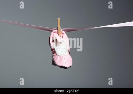 Eine Nahaufnahme von kleinen rosa Ballettschuhen, die auf einem rosa Band auf einem grauen Hintergrund hängen Stockfoto