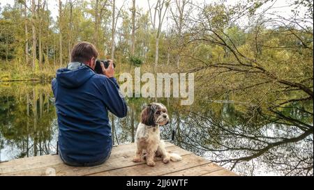 Ein Fotograf mit seinem niedlichen Shih Tzu Hund, der Fotos vom Teich machte Stockfoto