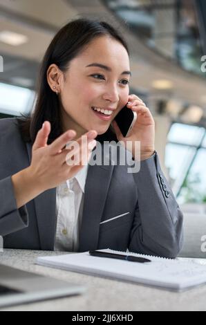 Glückliche junge chinesische Geschäftsfrau, die im Büro telefoniert. Stockfoto