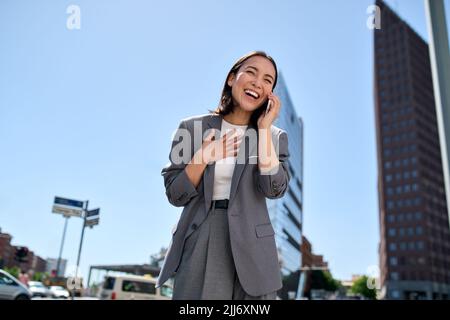 Junge, fröhliche asiatische Geschäftsfrau, die auf dem Handy lachte und auf der Straße lachte. Stockfoto