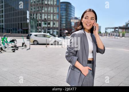 Junge glückliche asiatische Geschäftsfrau trägt Anzug und telefoniert auf der Straße der Stadt. Stockfoto