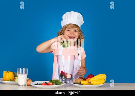 Kinderkoch isoliert auf blau. Lustige kleine Koch Koch Koch tragen einheitliche Kochmütze und Schürze gekochte Speisen mit Spinat in der Küche. Stockfoto