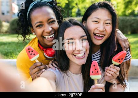 Eine Gruppe von drei multirassischen Frauen, die im Sommer Selfie beim Essen von Eis machen Stockfoto