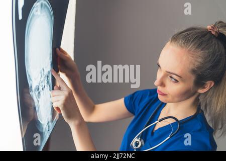 Professionell gekleidete kaukasische Neurologen, die auf eine Schädelröntgenaufnahme schaut und auf den Bereich zeigt, der gebrochen zu sein scheint. Grauer Hintergrund. Hochwertige Fotos Stockfoto