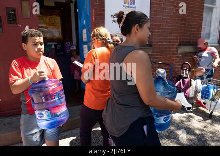 Newark, New Jersey, USA. 23.. Juli 2022. ANA HERREA und ihr Sohn MIKEUS aus Harrison, New Jersey, warten in der Schlange und tragen große Flaschen mit Wasserbehältern sowie zwei kleine Gallonen-Krüge in der St. Stephens Church, im Ironbound-Abschnitt von Newark, New Jersey. Die Newark Water Coalition gab eine unbegrenzte Versorgung mit frei gefiltertem Wasser aus. Herrara sagte, dass die Wasserversorgung der Familie für zwei Wochen andauern wird. (Bild: © Brian Branch Price/ZUMA Press Wire) Stockfoto