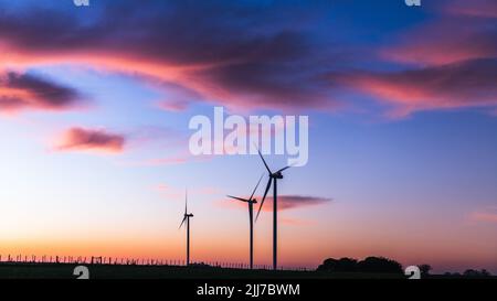 Silhouette von drei modernen Windmühlen unter einem bläulichen Sonnenuntergang am Stadtrand von Kiyú, San José, Uruguay Stockfoto