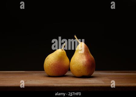 Paar Birnen auf Holzbrett vor schwarzem Hintergrund Stockfoto