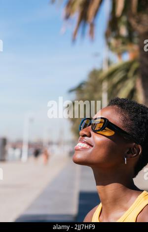 Vertikales Porträt von einer Seite einer positiven afrikanischen Frau mit sehr kurzen Haaren. Sie schaut weg und genießt die Sonne Stockfoto