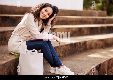 Nur zwischen den Klassen chillen. Porträt einer attraktiven jungen Universitätsstudentin, die während ihrer Pause draußen auf dem Campus sitzt. Stockfoto