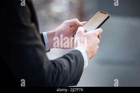 Nur ein moderner Geschäftsmann, der moderne Geschäfte macht. Ein nicht erkennbarer Geschäftsmann, der in der Stadt steht und sein Handy benutzt. Stockfoto