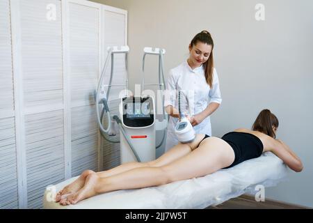 Frau, die wegen Cellulite behandelt wird. Schlankheits-Vakuum-Massage-Maschine. Vakuummassage von Gesäß und Beinen. Anti-Cellulite Körperformungsverfahren. Junge Frau und Arzt im Medizinsalon Stockfoto