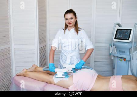 Vakuummassagegerät. Vakuummassage von Gesäß und Beinen. Anti-Cellulite Körperformungsverfahren. Schlankheits-Maschine. Junge Frau und Arzt im Medizinsalon Stockfoto