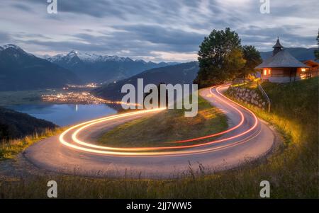 Die leichten Wege von Autos auf einer Straße zum Wasser und beleuchteten Gebäude umgeben von Bergen in Zell am See, Österreich Stockfoto