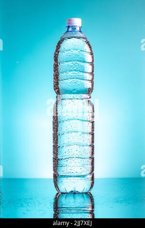 Kalte Plastikflasche mit Wassertropfen auf blauem Hintergrund. Stockfoto