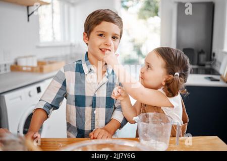 Du hast etwas auf deine Nase bekommen... ein kleines Mädchen und ein kleiner Junge, die Spaß haben, während sie zu Hause zusammen backen. Stockfoto