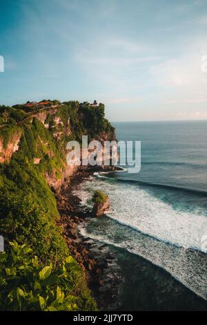 Die sanften Meereswellen mit Schaum auf den Felsen an der riesigen Klippe des Uluwatu-Tempels in Bali, Indonesien Stockfoto