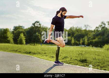 Sportler Mann mit Behinderungen - eine Beinprothese - macht Stretching- und Warming-Übungen für sein Training im Freien im Park Stockfoto