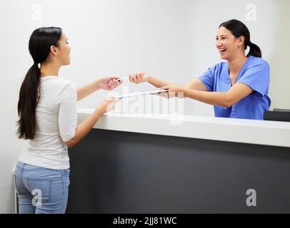 Unsere nie ganz gekleidet ohne ein Lächeln. Ein Patient und Assistent in einem Zahnarztbüro interagieren. Stockfoto