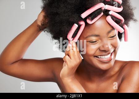Meine Haare lieben das. Eine junge Frau stylt ihre Haare vor einem grauen Hintergrund. Stockfoto