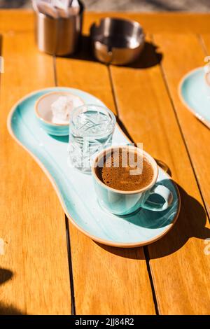 Eine Tasse heißen schwarzen türkischen Kaffee in einer blauen Tasse serviert mit einem Glas Wasser und Zucker Stockfoto