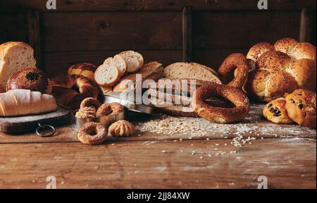 Scheiben frisch gebackenes türkisches Brot mit verschiedenen süßen Gebäckstücken, serviert auf einem unordentlichen Holztisch mit Haferbrei in einer leichten Bäckerei Stockfoto