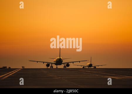 Passagierflugzeuge starten vor dem Hintergrund eines malerischen Abendhimmels mit Sonnenstrahlen von der Start- und Landebahn des Flughafens. Stockfoto