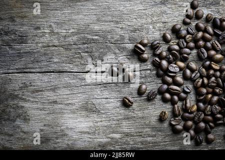 Bild von Kaffeebohnen, die auf Holzboden auf einem dunklen Hintergrund mit Kopierfläche gestapelt sind Stockfoto