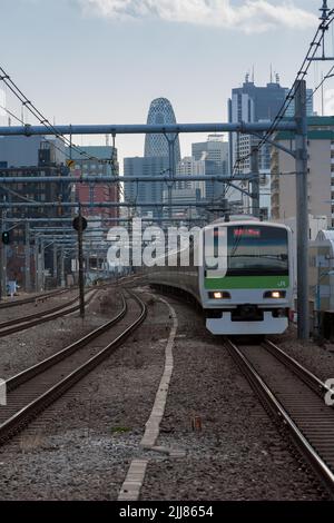 Ein Zug der Serie E231-500 auf der JR Yamanote-Linie vor der Shinjuku-Skyline mit dem Cocoon Tower im Zentrum von Tokio, Japan. Stockfoto