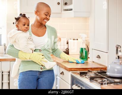 Sein Arbeitstag. Eine attraktive junge Frau trägt ihre Tochter, während sie zu Hause die Arbeit verrichten. Stockfoto