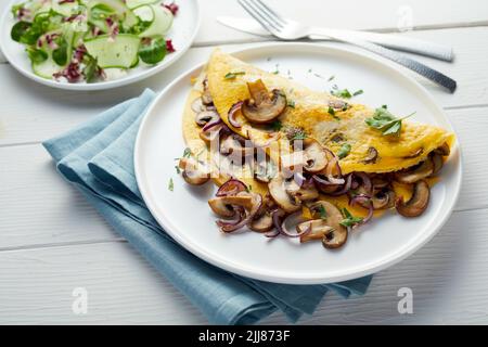 Hoher Winkel von Omelette mit Pilzen und Petersilie auf den Tisch mit Gemüsesalat für leckeres Mittagessen gelegt Stockfoto
