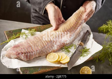 Von oben Ernte unkenntlich männlicher Koch mit rohem Fischfilet auf Schneidebrett mit Zitrone und Dill in der Küche platziert Stockfoto