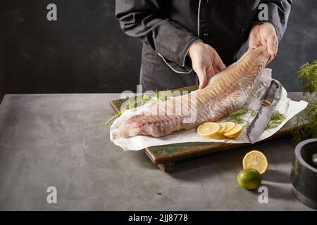 Hoher Winkel der Ernte gesichtslosen männlichen Koch am Tisch stehend mit rohem frischem Fischfilet in der Küche Stockfoto