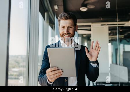 Glücklicher kaukasischer Geschäftsmann im Anzug, der im Büro arbeitet, mit Geschäftspartnern über ein digitales Tablet chatten kann Stockfoto