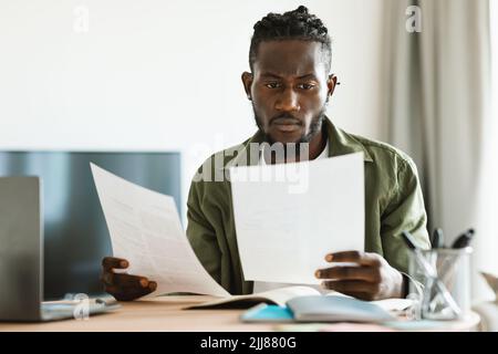 Fernkarriere, Konzept für freiberufliche Tätigkeit. Fokussierter schwarzer Mann, der zu Hause arbeitet und Geschäftsdokumente durchschaut Stockfoto