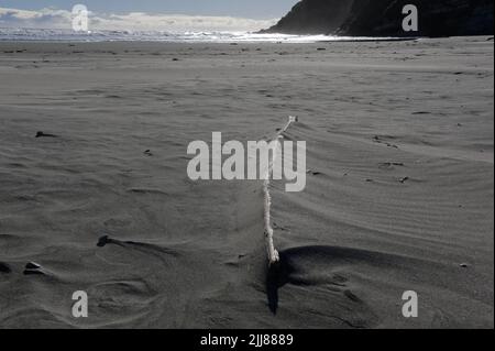 Sand hat sich auf einem großen Stück Treibholz an einem Strand aufgebaut. Windmuster werden um Steine im Sand gezeigt. Stockfoto