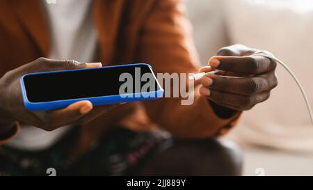 Schwarze männliche Hände stecken ein Ladegerät in moderne Smartphone, mit Powerbank, Nahaufnahme Stockfoto