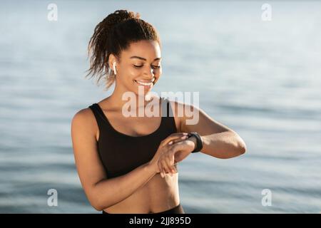 Schwarze Frau verfolgt ihre Outdoor-Aktivitäten und schaut auf Smart Watch Stockfoto