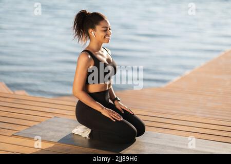 Friedliche afroamerikanische Frau, die am Strand meditiert Stockfoto