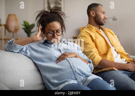 Unglücklich Schwanger Schwarze Frau Sitzt In Der Nähe Indifferent Mann Zu Hause Stockfoto